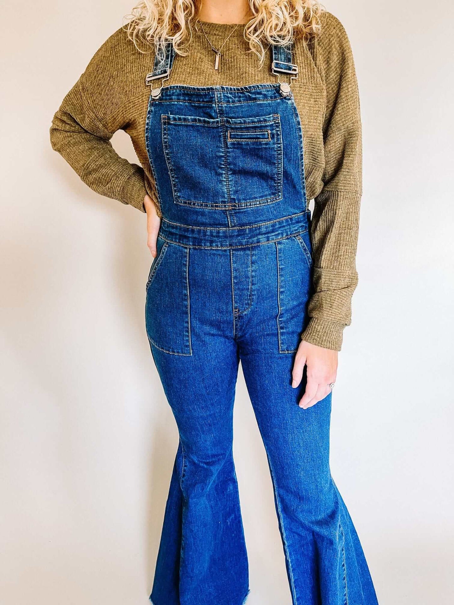 Stylish model wearing blue denim flare overalls paired with a mustard-colored sweater, completing the outfit with a trendy wide-brim hat and pointed-toe booties, creating a chic and modern look