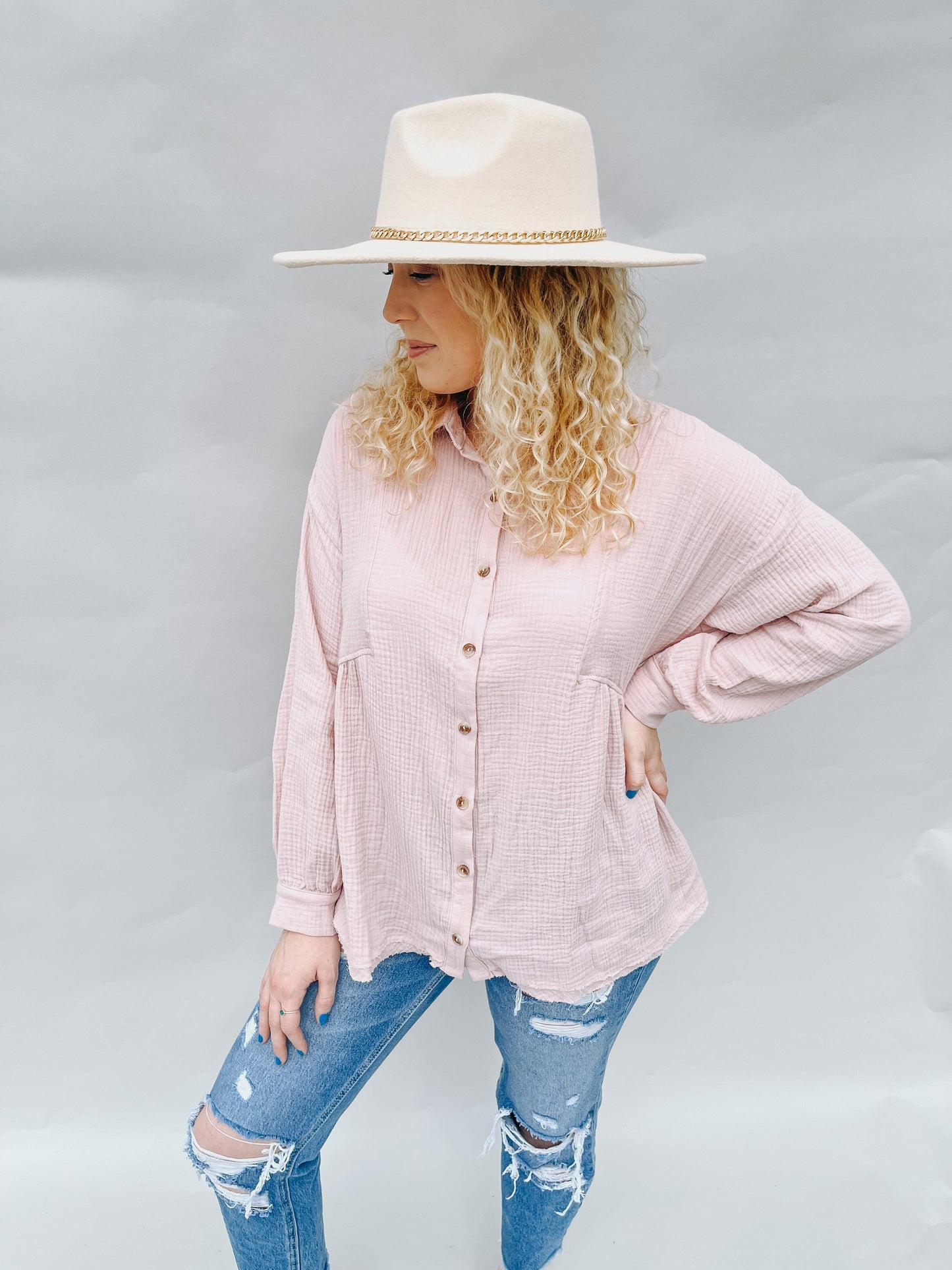 Fashionable model wearing a light pink linen button-up shirt, paired with distressed jeans and a wide-brim hat, exuding a relaxed and trendy vibe