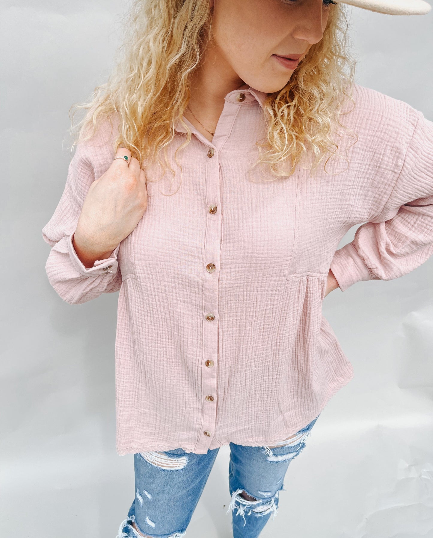 model wearing a light pink linen button-up shirt, paired with distressed jeans and a wide-brim hat, exuding a relaxed and trendy vibe."