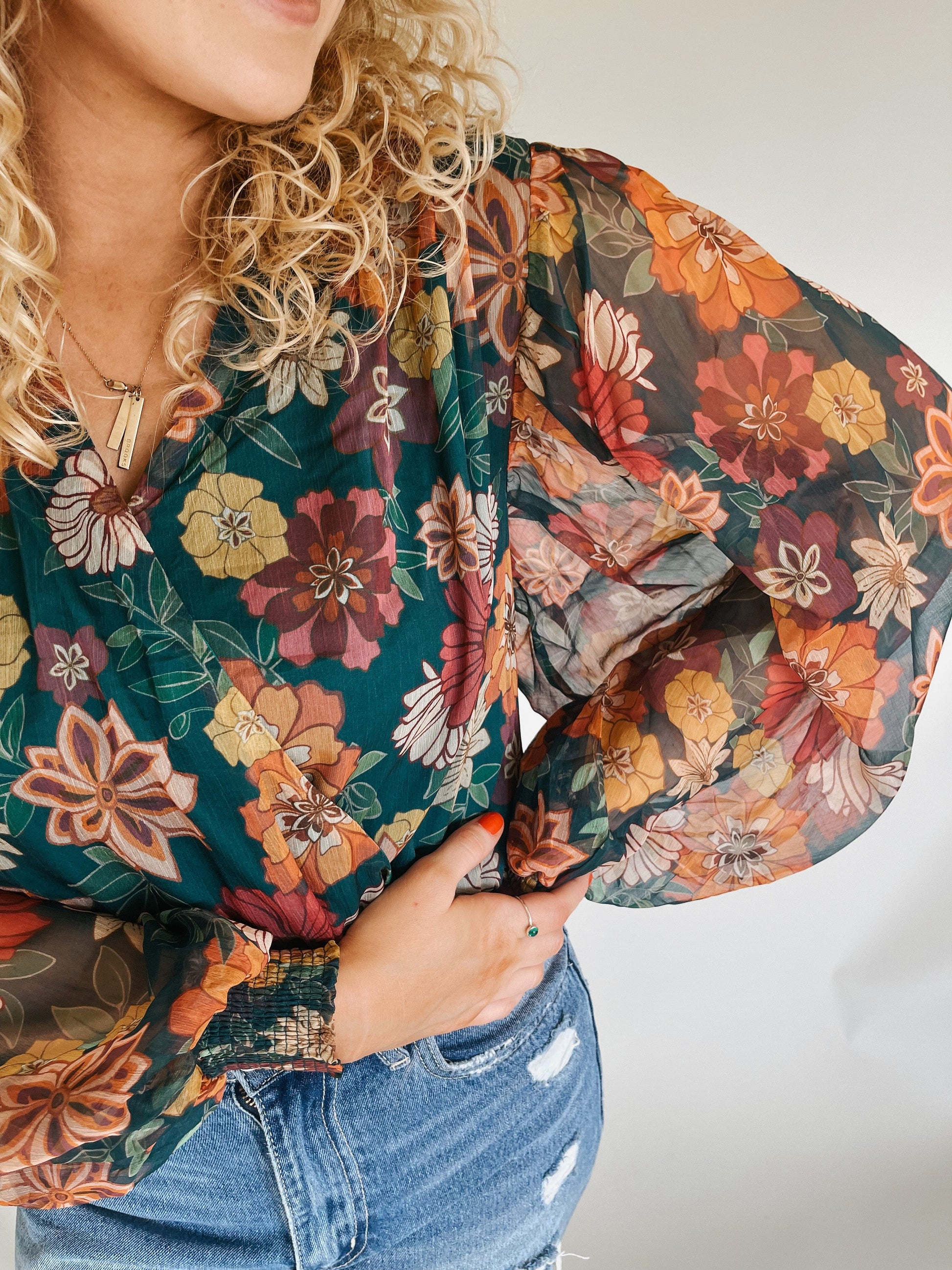 Close-up image of the intricate floral pattern on a green, orange, and red bodysuit with flowy sleeves, showcasing the vibrant colors and delicate details of the design."