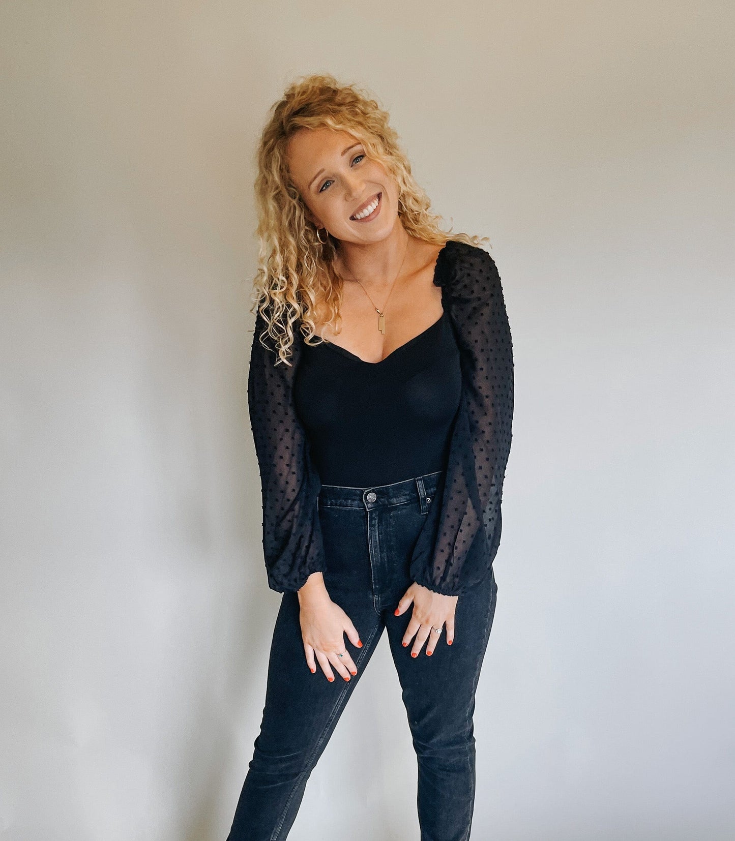Smiling model wearing a black bodysuit and black jeans poses for the camera, exuding confidence and style.